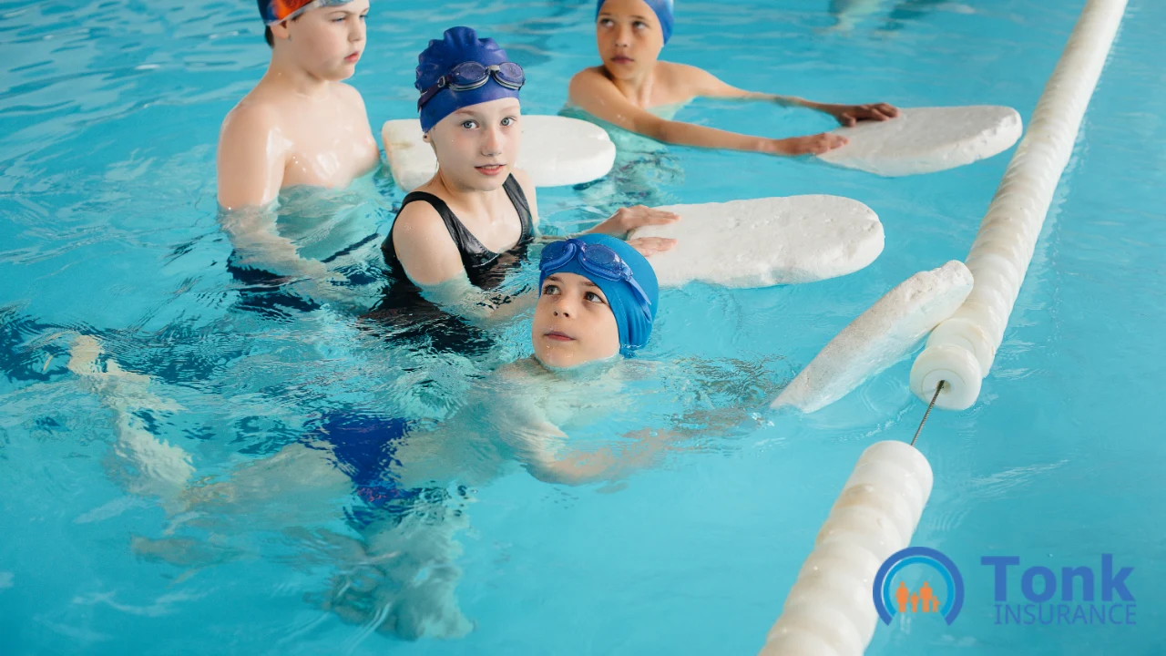 Children in swim caps holding kickboards at the lane rope during a swim school group lesson